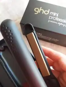 Mano sosteniendo la plancha de pelo GHD Mini Styler con caja en el fondo